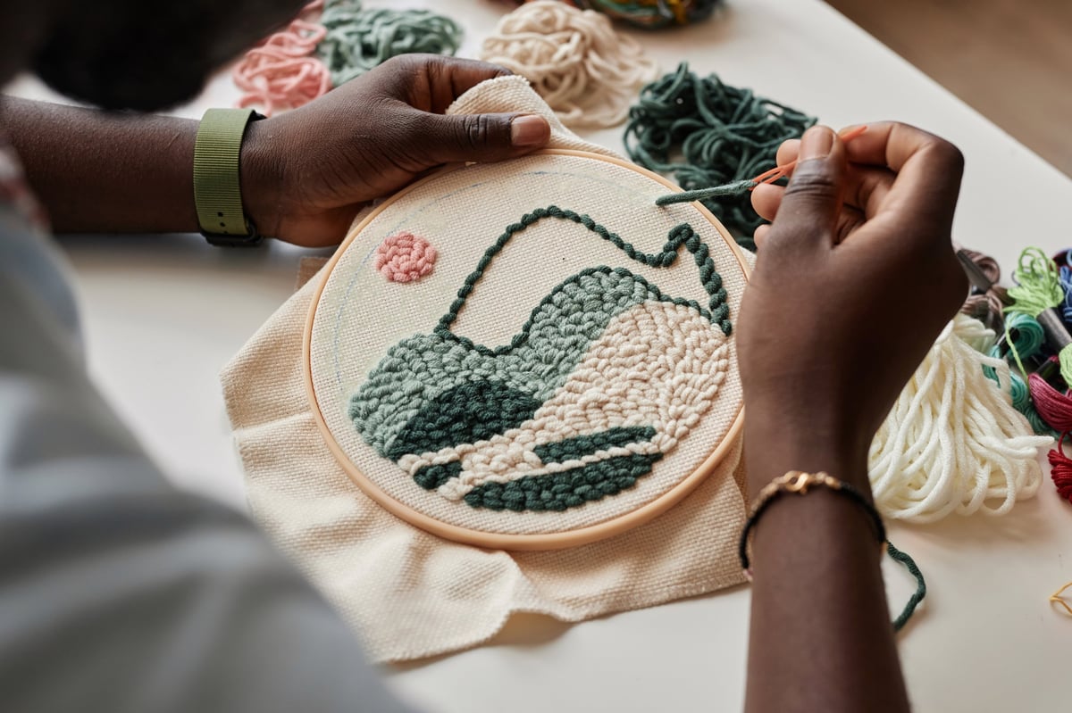 Artesano joven creando bordado punch needle sobre tela blanca con hilos especiales
