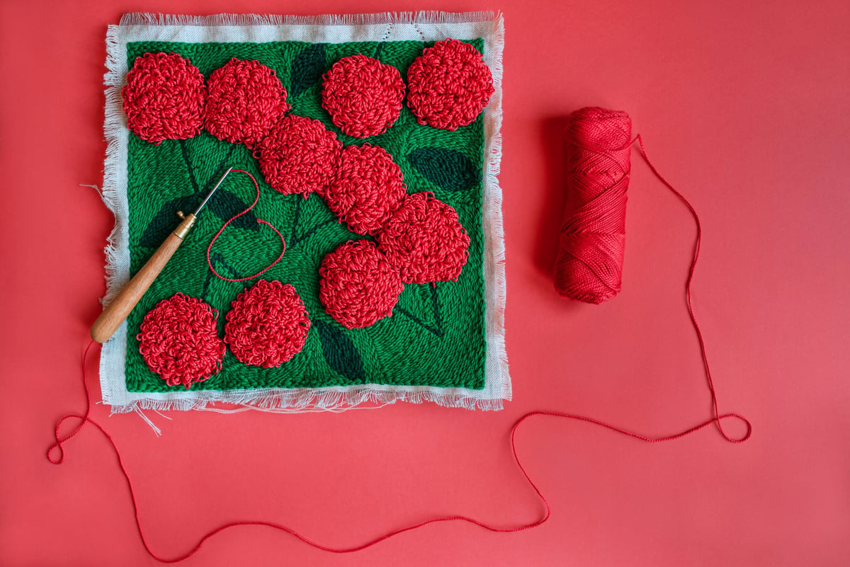 Bordado punch needle de flores rojas sobre tela con lana roja y aguja mágica