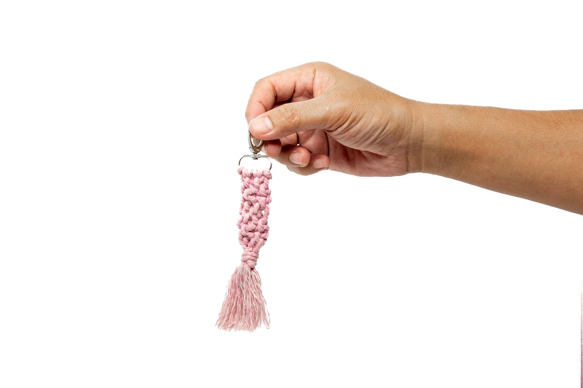 Mano sosteniendo llavero de macramé sobre fondo blanco