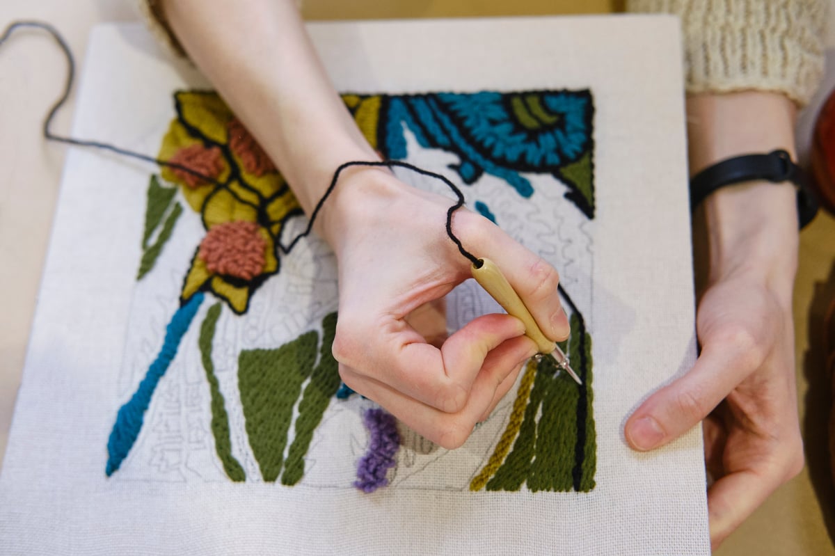 Manos creando bordado floral punch needle colorido sobre tela con herramienta de madera