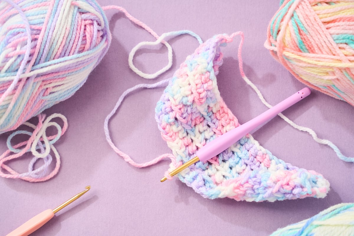 Proyecto de crochet en progreso con lana pastel y aguja de ganchillo