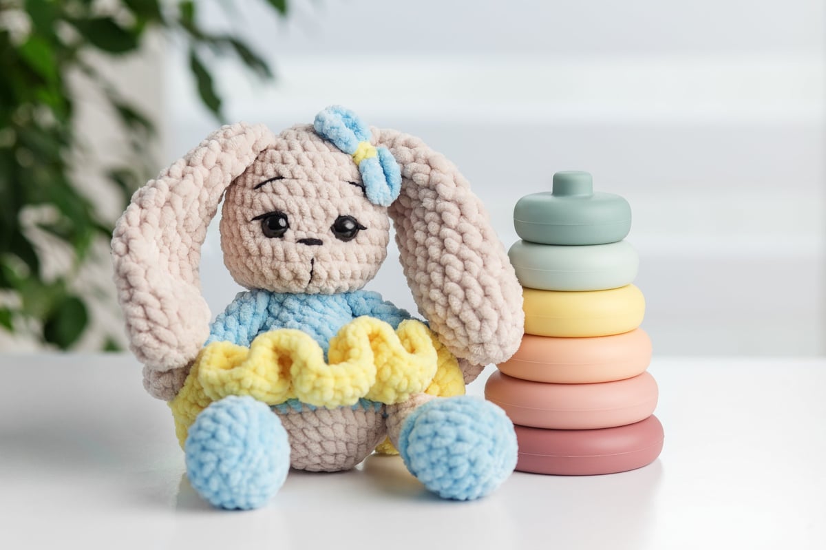 Amigurumi tejido a crochet: conejito de peluche hecho a mano junto a aros apilables pastel