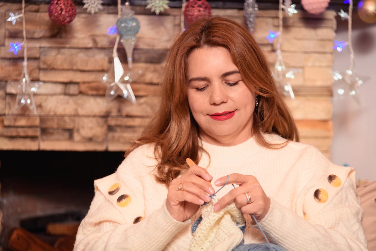 Mujer tejiendo crochet junto a la chimenea en ambiente acogedor