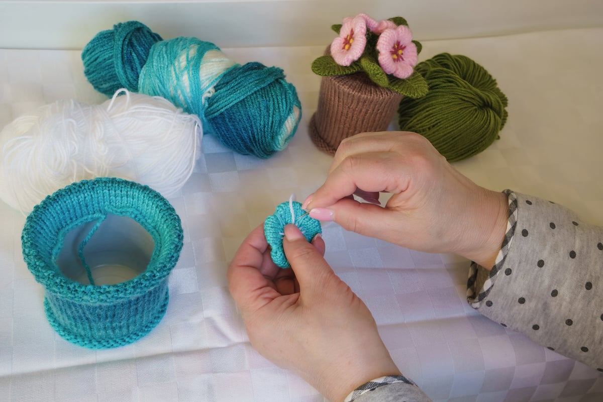Manos tejiendo amigurumi con lanas de colores sobre mesa de trabajo