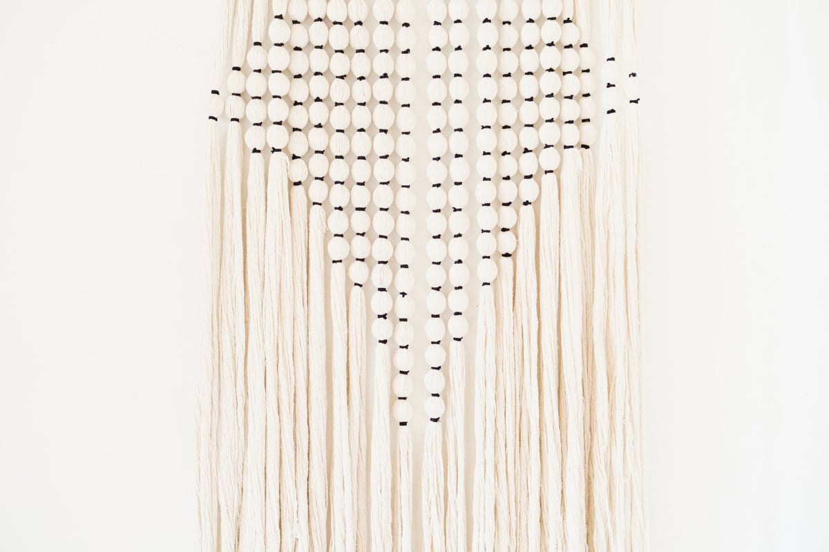 Tapiz de macramé crema con cuentas negras en forma de diamante sobre fondo blanco