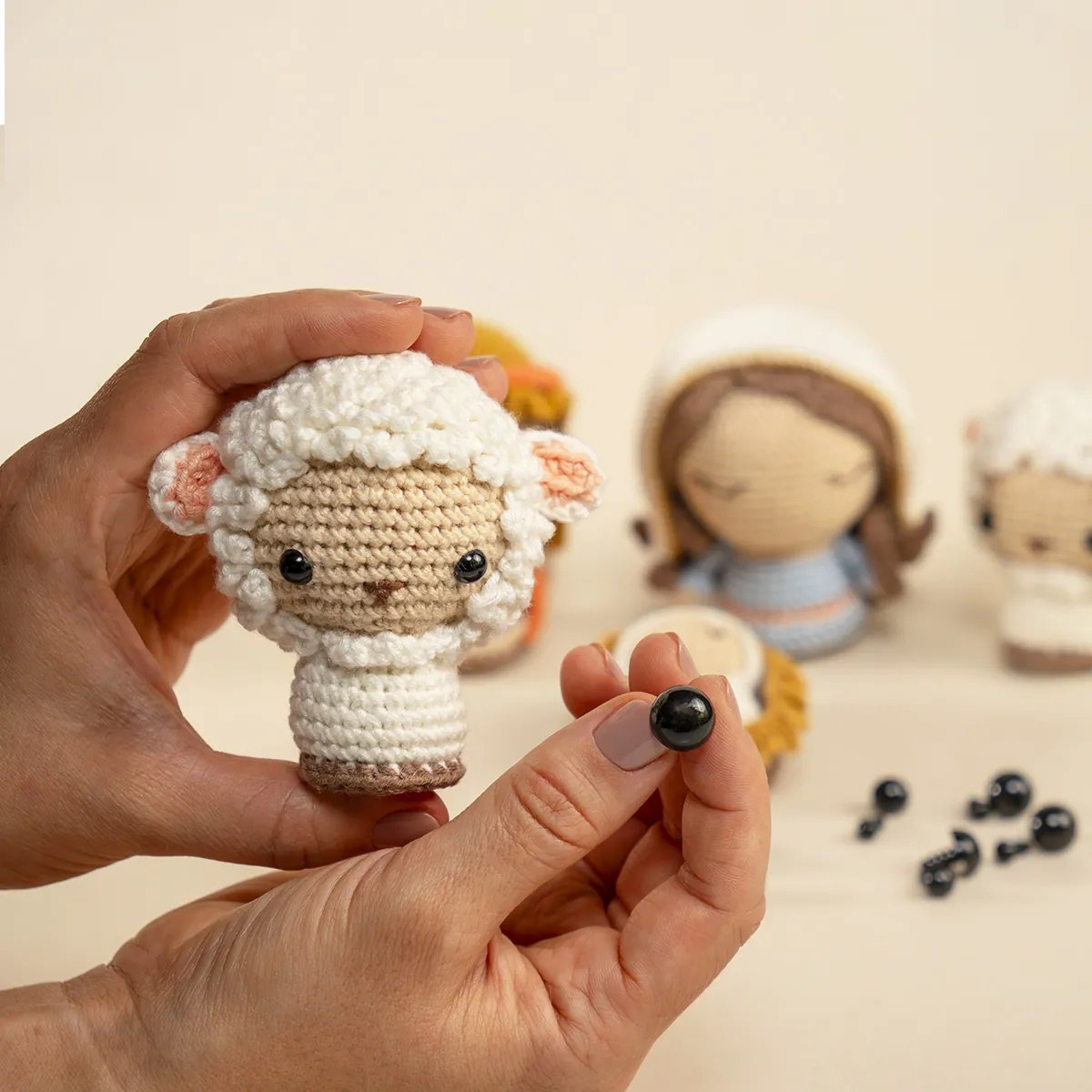 Ojos de seguridad negros pequeños sostenidos en la mano junto a un amigurumi de oveja tejido en crochet