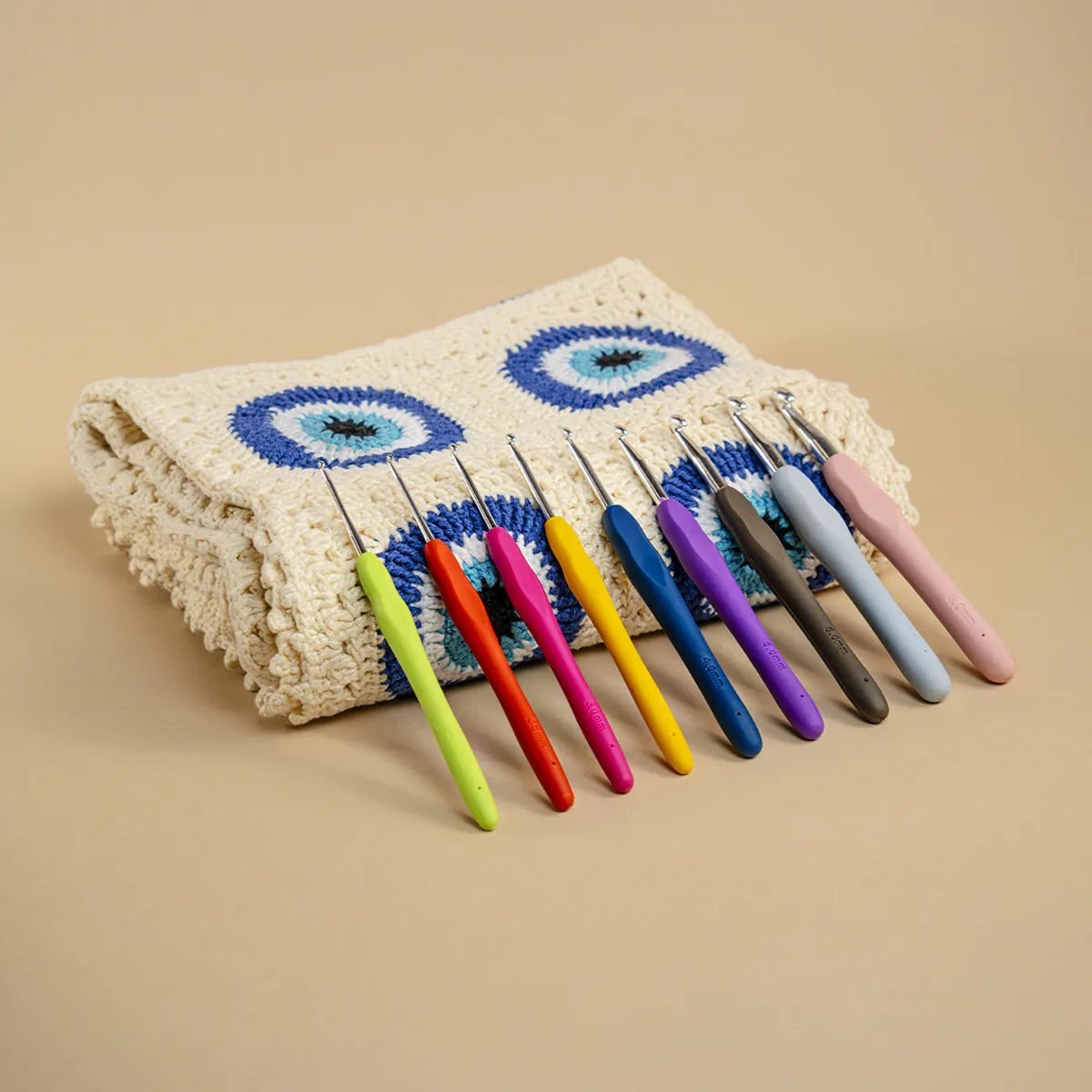 Juego de agujas de crochet de colores en diferentes tamaños sobre una carpeta tejida al crochet con motivos de ojos