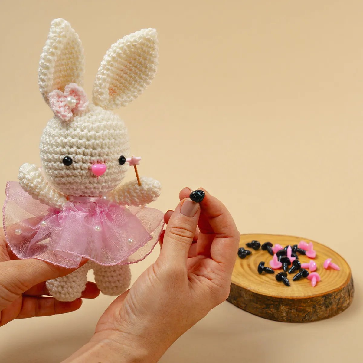 Narices de seguridad rosadas y negras en mini tabla de madera junto a amigurumi de conejita con tutú rosa