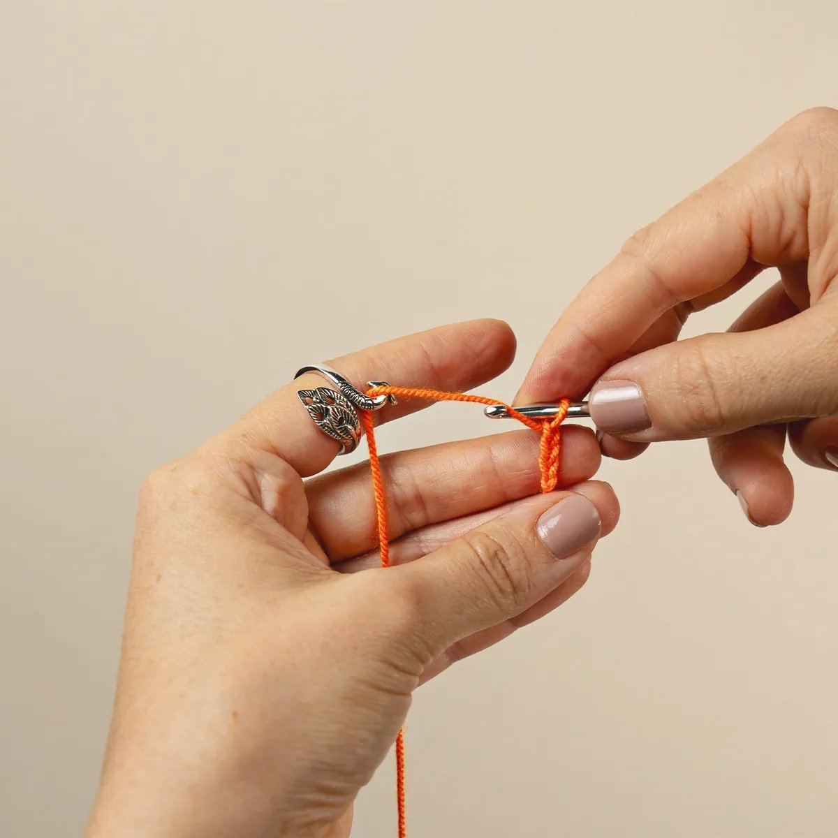 Anillo decorativo plateado en forma de pavo real usado como guía para tejer crochet con hilo naranja