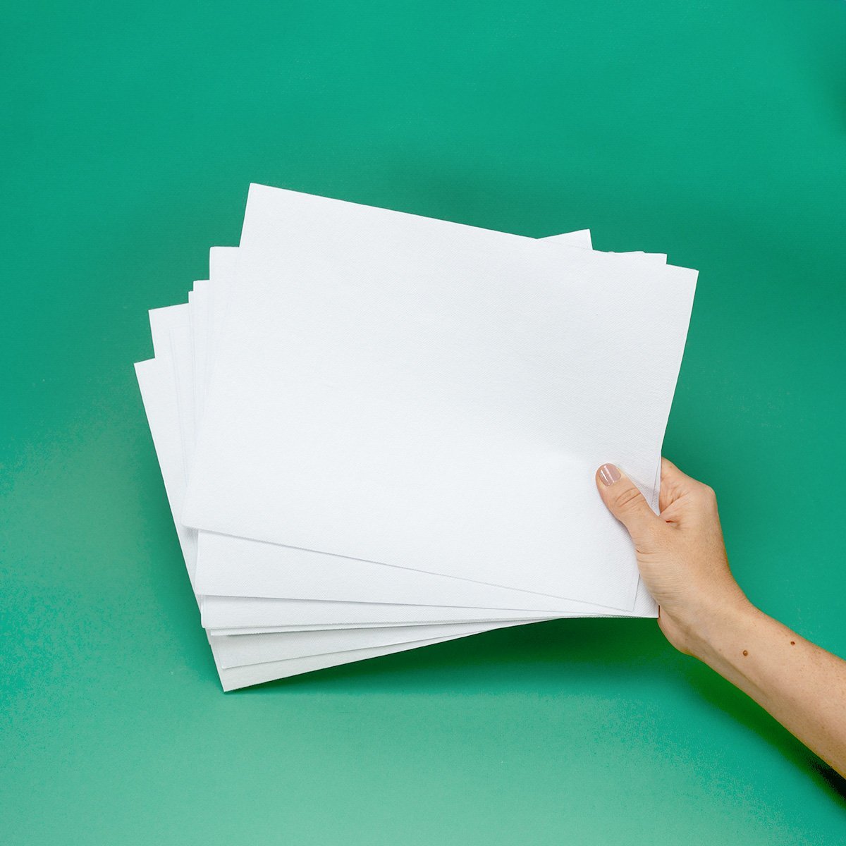 Mano sosteniendo un mazo de papeles blancos lisos — tela hidrosoluble para bordado y punch needle sobre fondo verde turquesa