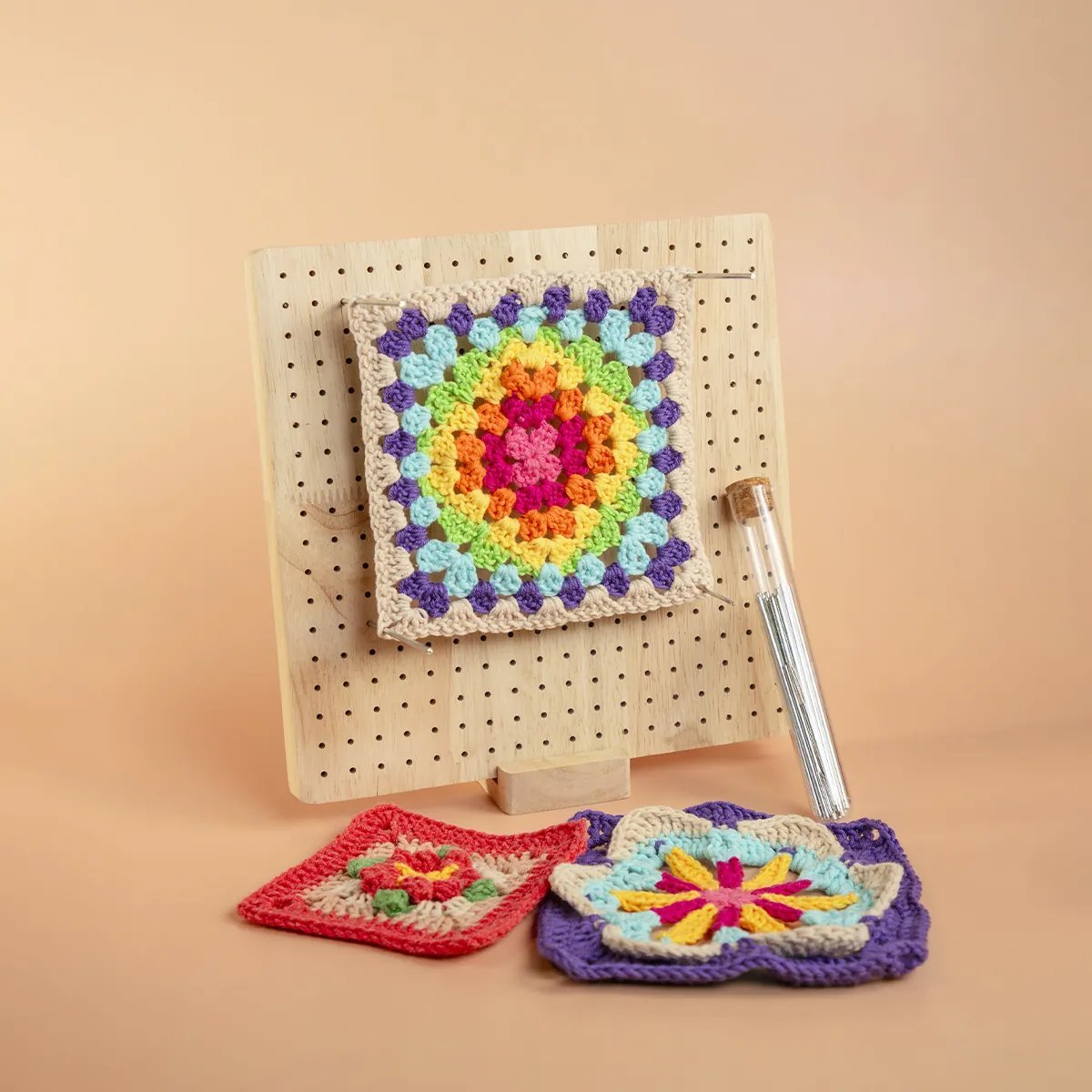 Tabla de bloqueo para granny squares de madera con un granny colorido bloqueado y dos cuadritos terminados al lado