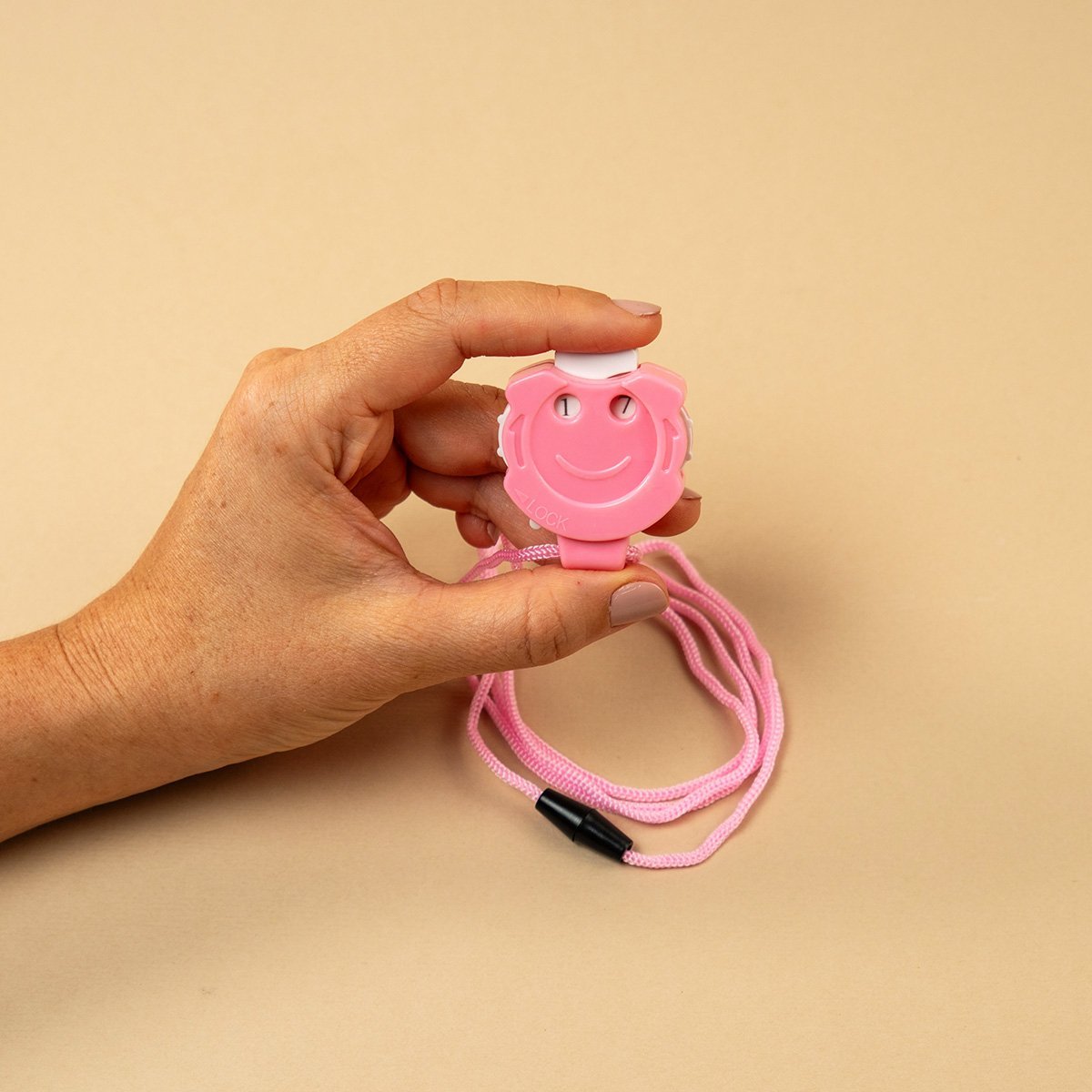 Contador de vueltas manual en forma de cara feliz color rosa con cordón rosa sostenido en la mano