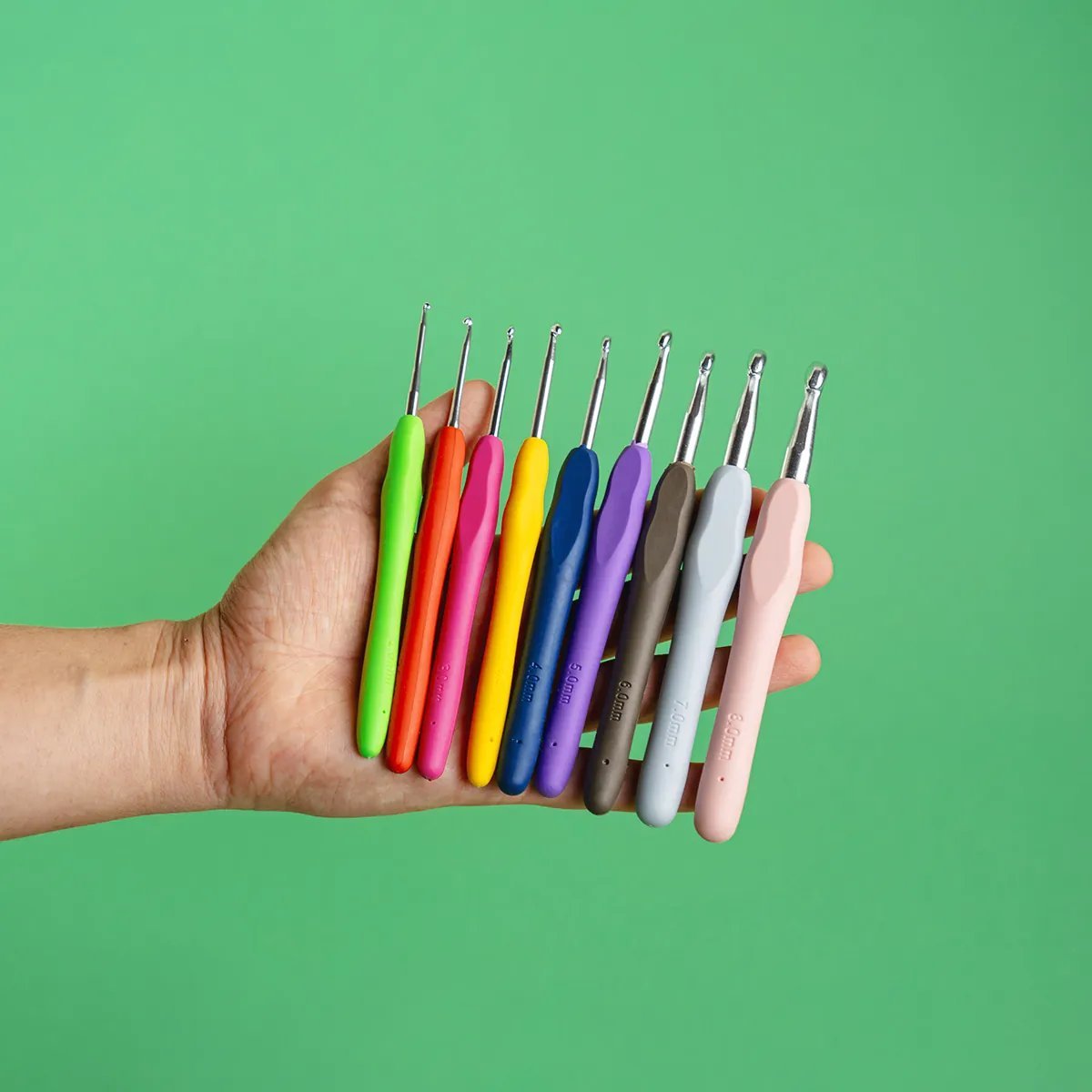 Set de agujas de crochet de colores en diferentes tamaños (3mm a 8mm) sostenidas en una mano