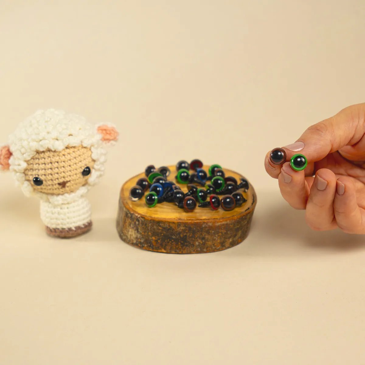 Ojos de seguridad de colores en diferentes tonos sostenidos junto a un amigurumi de oveja tejido a crochet